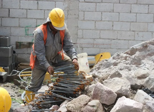 Albañil con casco y chaleco preparando armaduras de acero entre escombros en una obra de ampliación en Maracena