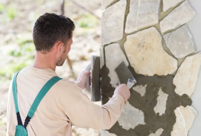 Albañil colocando piezas irregulares de piedra caliza en la fachada de una vivienda en Pinos Genil