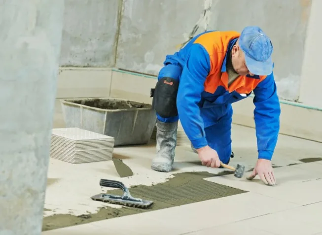 Albañil colocando baldosas de gres porcelánico sobre una base regularizada en una vivienda de La Chana